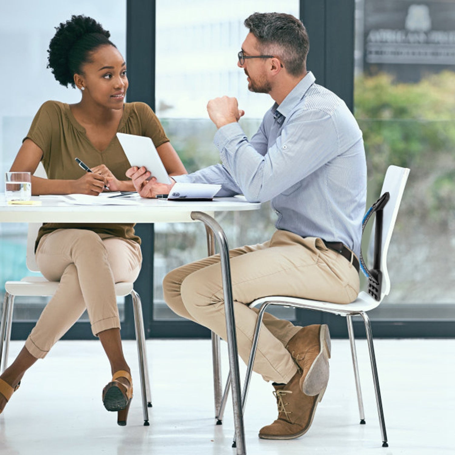 Two professionals discussing business at a modern office table with tablet and documents